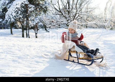 Bambino seduto sulla slitta in un parco cittadino innevato durante le soleggiate giornate invernali Foto Stock