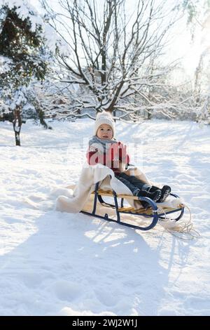 Bambino seduto sulla slitta in un parco cittadino innevato durante le soleggiate giornate invernali Foto Stock