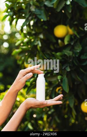 La donna tiene tra le mani una bottiglia di prodotto per la cura della pelle sullo sfondo di limoni. Foto Stock