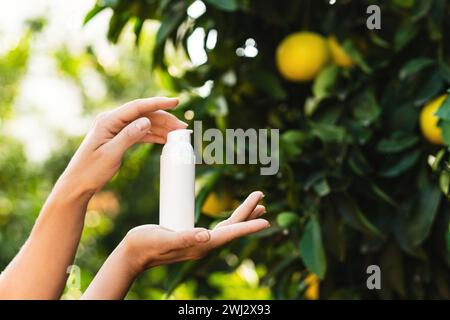 La donna tiene tra le mani una bottiglia di prodotto per la cura della pelle sullo sfondo di limoni. Foto Stock