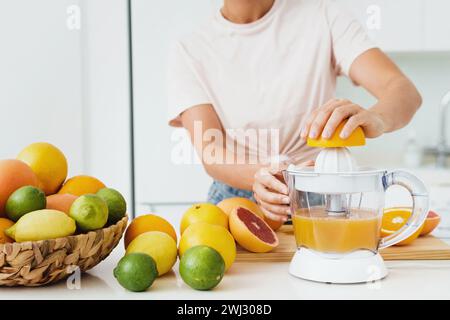 Mani femminili e spremiagrumi durante la preparazione del succo d'arancia fresco Foto Stock