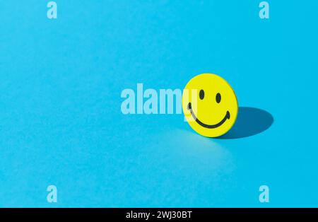 Layout creativo realizzato con adesivo smiley su sfondo blu. Pensiero positivo minimo e concetto di buon umore. Foto Stock