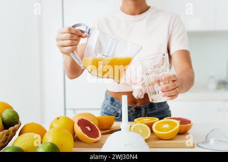 Donna che versa nel bicchiere succo d'arancia appena spremuto in casa Foto Stock