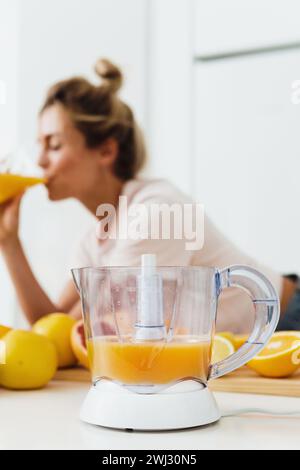 Spremiagrumi e donna che beve succo d'arancia appena spremuto in casa Foto Stock