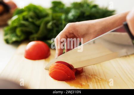 Mani femminili con coltello che affetta pomodoro rosso su un tagliere di legno Foto Stock