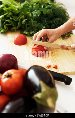 Mani femminili con coltello che affetta pomodoro rosso su un tagliere di legno Foto Stock