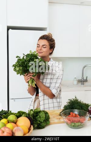 Donna con un mucchio di coriandolo verde durante la cottura in cucina Foto Stock