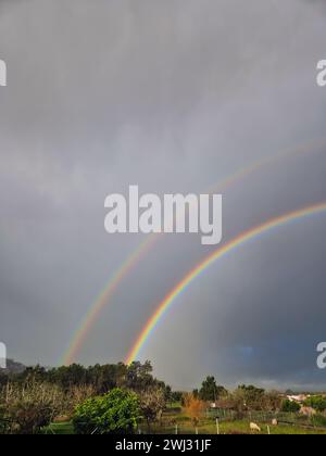 Un doppio arcobaleno sopra un campo agricolo. Due archi colorati nel cielo nuvoloso e scuro nella campagna del Portogallo. Foto verticale Foto Stock
