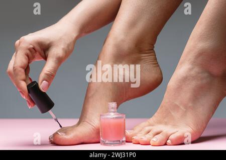 Piede femminile con una bella pedicure francese. Donna che applica smalto rosa sulle unghie dei piedi. Foto Stock