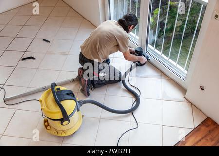 L'uomo sta lavorando con un Grinder. Levigatura della superficie del pavimento per piastrelle mediante rettificatrice elettrica per pavimenti Foto Stock