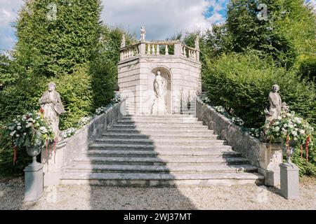 Mazzi di fiori in antichi vasi in pietra e lungo il corrimano della scalinata fino alla statua della ninfa nel giardino Foto Stock