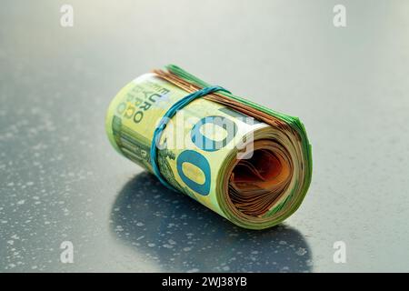 I soldi tirano l'euro isolato su un tavolo buio. Banconote da 100 e 50 Euro attorcigliate nel tubo e legate Foto Stock