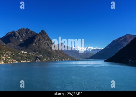 Vista sul lago di Lugano con verdi colline e cime innevate sotto un cielo blu Foto Stock