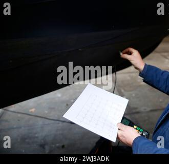 Un tecnico addetto alla manutenzione che misura lo spessore dello scafo in acciaio di un'imbarcazione utilizzando un dispositivo a ultrasuoni Foto Stock