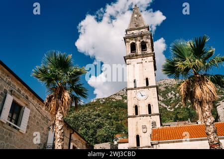 Campanile della Chiesa di S.. Nicola con un orologio tra antiche case sullo sfondo di verdi montagne. Perast, Mont Foto Stock