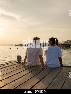 Coppia seduta su un molo di legno nell'oceano durante il tramonto a Samaesan in Thailandia Foto Stock