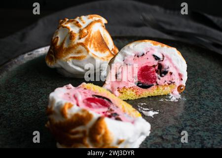 Mini Alaska cotta a fette con un Cherry Center: Una tazza di gelato rosa con gocce di cioccolato su una torta di spugna circondata da meringa incendiata Foto Stock