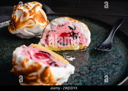 Mini Alaska cotta a fette con un Cherry Center: Una tazza di gelato rosa con gocce di cioccolato su una torta di spugna circondata da meringa incendiata Foto Stock