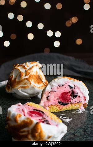 Mini Alaska cotta a fette con un Cherry Center: Una tazza di gelato rosa con gocce di cioccolato su una torta di spugna circondata da meringa incendiata Foto Stock