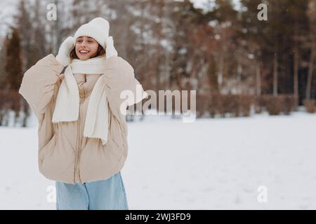 Felice sorridente giovane donna vestito da ritratto sciarpa cappello e guanti gode del tempo invernale nella foresta invernale innevata. Foto Stock