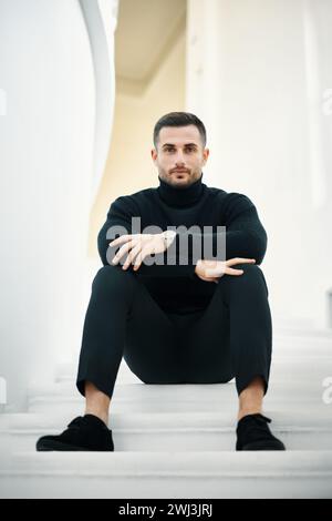 Ritratto di un bel giovane uomo in abito nero su un moderno sfondo bianco Foto Stock