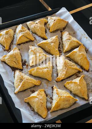 Le torte triangolari per pasta sfoglia con semi di sesamo si trovano su un vassoio sul tavolo Foto Stock