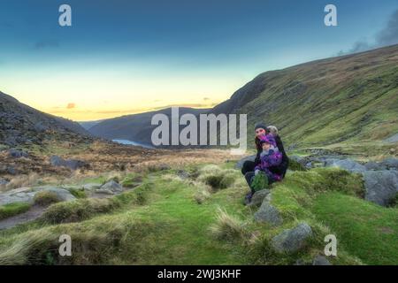 Madre e figlia sedute su una pietra a Glendalough al tramonto. Escursioni nelle splendide montagne autunnali di Wicklow, Irlanda Foto Stock