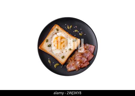 Uovo fritto a forma di cuore nel pane tostato con semi di sesamo, semi di lino e semi di zucca su un piatto nero Foto Stock