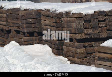 Pile di vecchie traversine in legno d'epoca circondate dalla neve Foto Stock