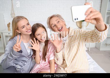 Bambina con la mamma e la nonna che si fanno selfie in camera da letto Foto Stock