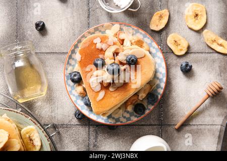 Piatto con gustosi pancake a forma di cuore, banana secca, mirtillo e miele su sfondo piastrellato grigio. Festa di San Valentino Foto Stock