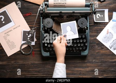 Mano femminile con macchina da scrivere vintage, manette e fascicoli criminali su sfondo in legno Foto Stock