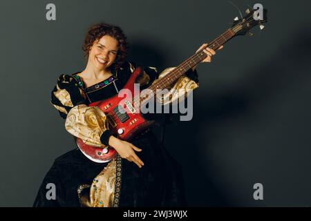 Ritratto di una giovane donna adulta che suona musica con la chitarra elettrica e indossa un abito medievale. Foto Stock