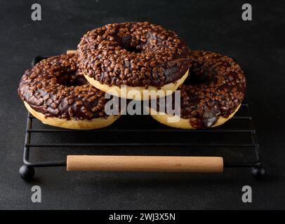Ciambelle al cioccolato cosparse di noci schiacciate su un tavolo nero Foto Stock