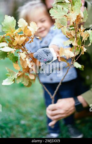 Papà tiene in mano un ramo di quercia e una bambina tiene in mano un gatto giocattolo Foto Stock