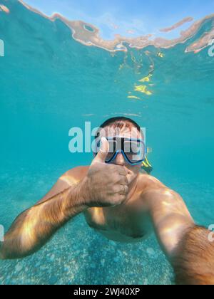 L'uomo con gli occhiali e le pinne nuota sott'acqua con il pollice in alto Foto Stock