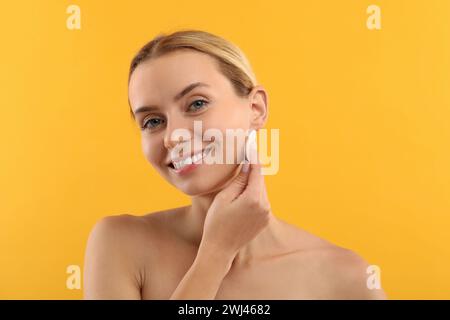 Donna sorridente che rimuove il trucco con un tampone di cotone su sfondo giallo Foto Stock