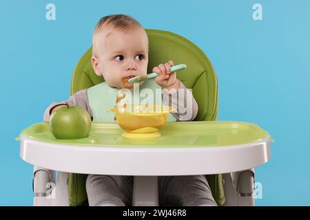 Piccolo bambino carino che mangia cibo sano in seggiolone su sfondo azzurro Foto Stock