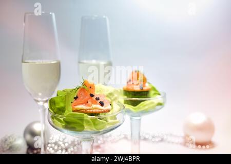 Antipasto di salmone affumicato con caviale e lattuga in bicchieri, due flute di champagne e decorazioni natalizie, snack per feste Foto Stock