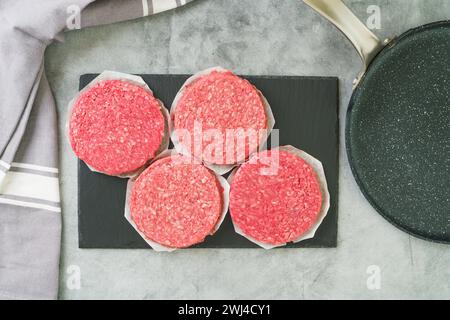 Polpettine di hamburger in plastica e primo piano di padella. Primo piano di polpettine fresche di hamburger crude su sfondo in pietra grigia, piano con spazio di copia Foto Stock