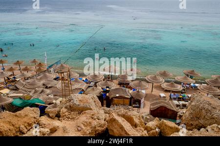 Vista dalla cima della spiaggia con ombrelloni di barche a canne e persone in piedi in acqua blu Foto Stock