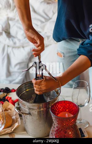 donna che apre una bottiglia di vino freddo nel secchiello dello champagne sul tavolino da caffè con spuntino Foto Stock