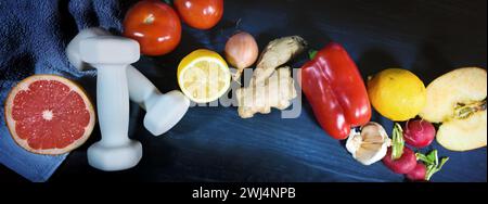 Manubri, verdura e frutta su sfondo di legno blu scuro, stile di vita sano con sport e cibo sano, panoramico Foto Stock