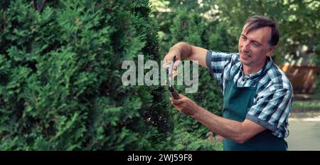 Uomo potatura albero con tagliatori. Maschio agricoltore taglia rami in giardino primaverile con cesoie per potatura o forbici Foto Stock