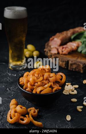 Spuntino all'orecchio di maiale nel recipiente da vicino con birra in un bicchiere Foto Stock