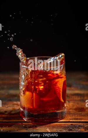 Cocktail alcolico Negroni o cocktail analcolico con spruzzo in bicchiere, bevanda con ghiaccio e buccia d'arancia come decorazione su legno Foto Stock