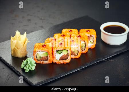 Sushi roll Philadelphia con tonno, avocado, formaggio spalmabile, cetrioli e caviale tobiko su sfondo scuro. Menu di sushi. Giapponese fo Foto Stock
