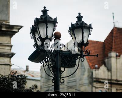 Lampione da strada con tre antiche lanterne stilizzate sullo sfondo di una casa fuori dal fuoco con un tetto marrone piastrellato Foto Stock