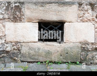 Antico muro di pietra fatto di grandi blocchi di pietra calcarea con una finestra dormitorio protetta da barre di ferro battuto Foto Stock