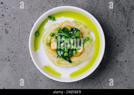 Purè di patate con burro, piselli verdi e basilico in un recipiente bianco Foto Stock